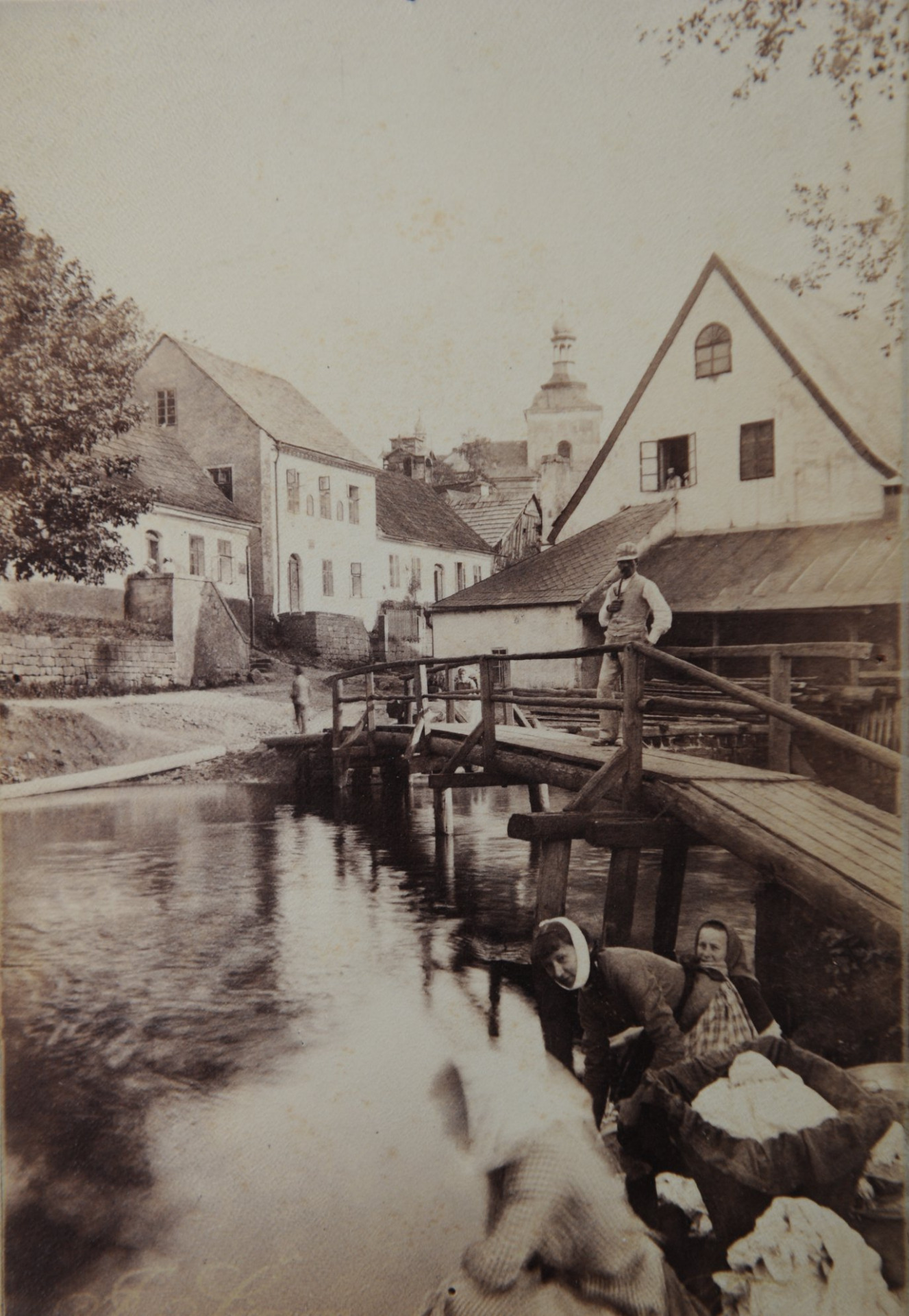 Na dnešní fotografii se podíváme do Konělup.👀 Fotografie zachycuje ženy při máchání prádla na Jizeře u Votrubcova mlýna. V pozadí je vidět kostel sv. Mikuláše. Před rozsáhlou přestavbou byl mlýn pana Emila Votrubce starým stavením s příkrou střechou, v zadní části s dřevěnou stavbou pro mlýnská kola, nad kterými byla ještě pila. V roce 1906 byla na místě mlýna vybudována elektrárna Emila Votrubce, kterou tam najdeme i dnes.😉 Foto: J. Šimon Zdroj: archiv Muzea Českého ráje v Turnově