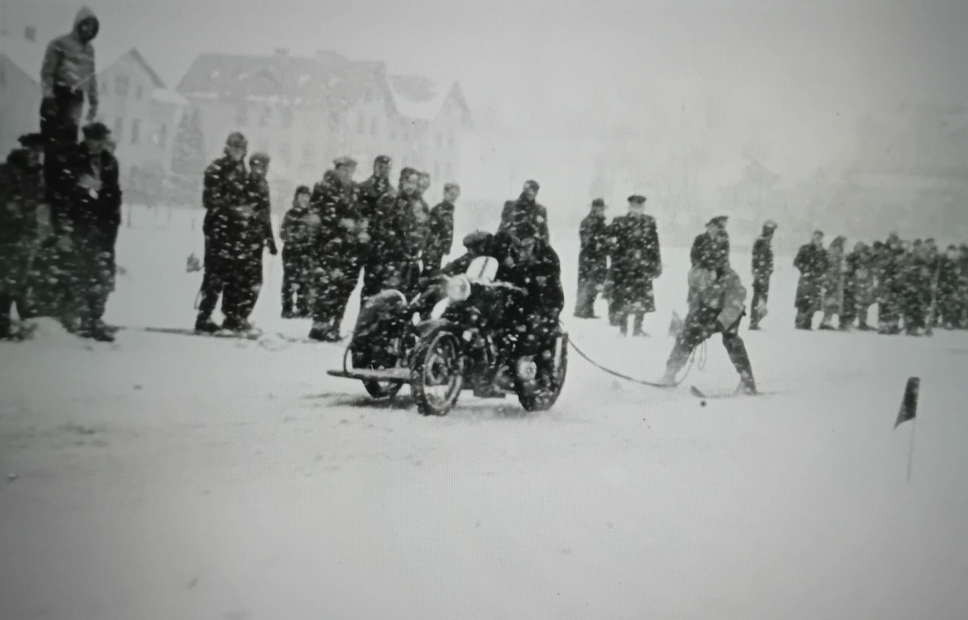 Motocykl se sajdkárou s číslem jedna a za ním jezdec na lyžích - tatínek Míly Jedličky ... vzadu budovy , to je tovární kolonie , matně úplně vzadu lze vytušit za lávkou přes Jizeru , hostinec " U Morávků " , už v Bítouchově ...