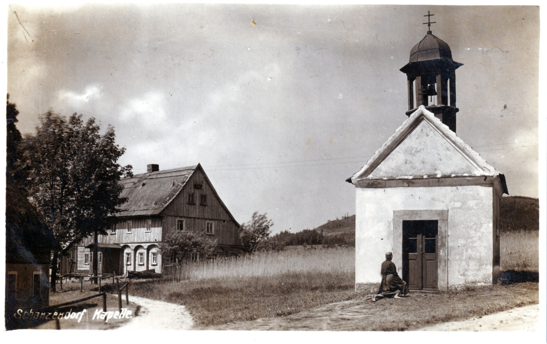 Tato pohlednice zachycuje kapli Navštívení panny Marie, která stála na severovýchodním okraji osady a po roce 1945 byla zbořena. Dnes už tu nenajdeme ani dvě sousední chalupy, patřící v době vzniku fotografie rodinám Kindermannů a Stengelů. (archiv Radim Nejedlý)